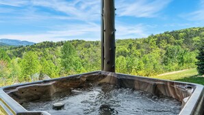 A hot tub with a wooden exterior, surrounded by a lush green landscape and a clear blue sky.
