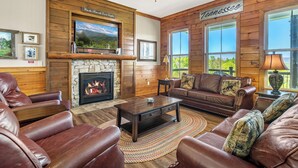 A cozy living room with leather furniture, a stone fireplace, and a large TV mounted above it.