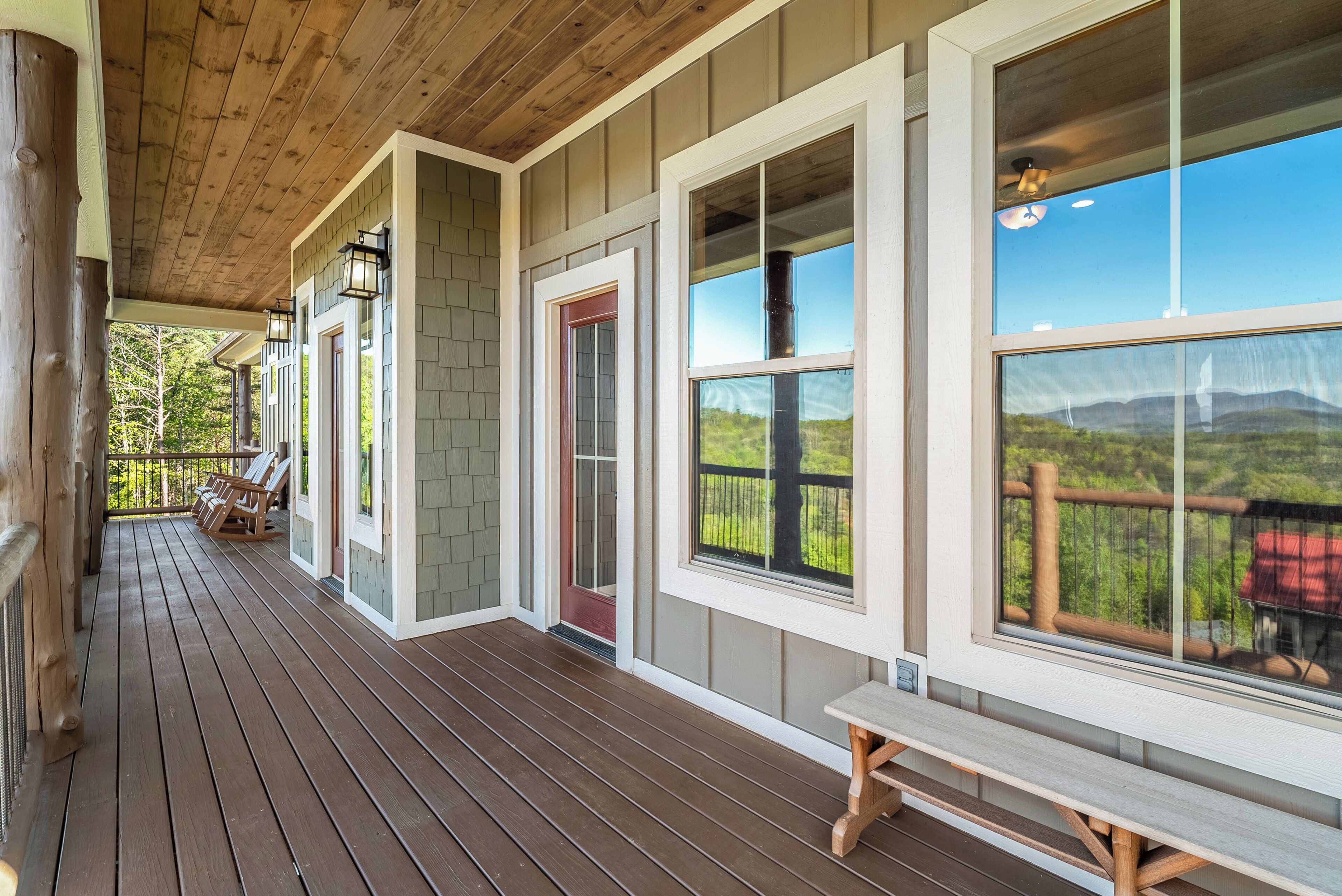 Um deck de madeira com um banco, janelas amplas e vista para a paisagem.