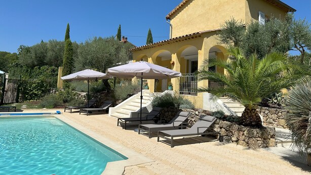 A poolside area with lounge chairs and umbrellas, a clear blue pool, and a yellow building with arches. - Villa Ocre, in Provence Verte, between the Mediterranean and the Gorges du Verdon. (Lorgues)