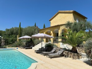 A poolside area with lounge chairs and umbrellas, a clear blue pool, and a yellow building with arches. - Villa Ocre, in Provence Verte, between the Mediterranean and the Gorges du Verdon. (Lorgues)