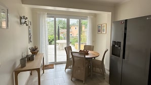A kitchen with a dining table, chairs, a refrigerator, and a view through the glass door. - Villa Ocre, in Provence Verte, between the Mediterranean and the Gorges du Verdon. (Lorgues)
