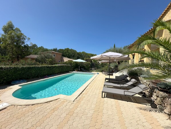 A rectangular swimming pool with a tiled edge, surrounded by a paved patio with hexagonal tiles. There are lounge chairs and umbrellas along the poolside. - Villa Ocre, in Provence Verte, between the Mediterranean and the Gorges du Verdon. (Lorgues)