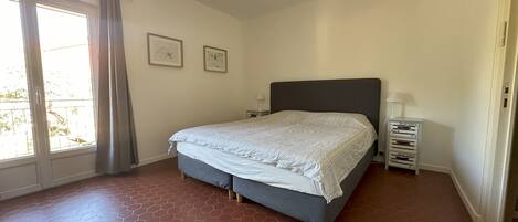 Un dormitorio con cama, ventilador de techo, ventana con cortinas y suelo de baldosas.