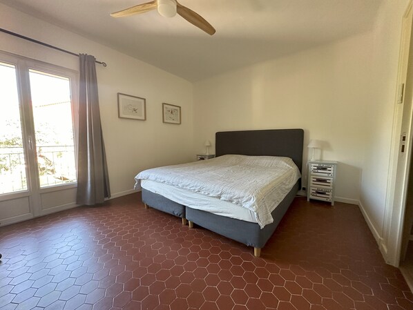 A bedroom with a bed, a ceiling fan, a window with curtains, and a tiled floor. - Villa Ocre, in Provence Verte, between the Mediterranean and the Gorges du Verdon. (Lorgues)
