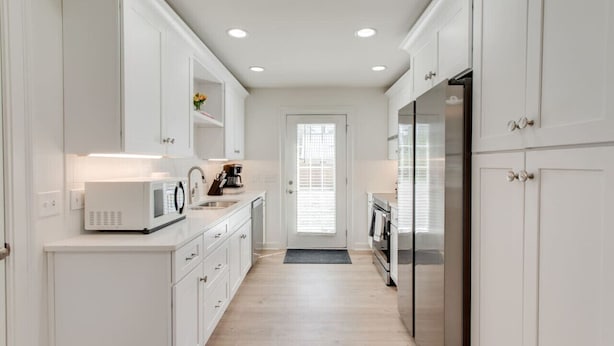 A narrow kitchen with white cabinetry, a microwave, a coffee maker, and a refrigerator. - Modern 4BR Home Near MTSU and Restaurants (Murfreesboro)