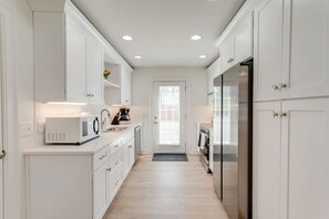Una cocina estrecha con armarios blancos, un microondas, una cafetera y un refrigerador.
