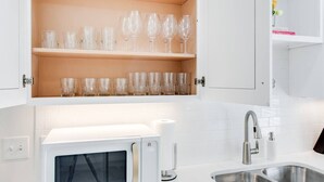 A kitchen with white cabinets, a microwave, a sink, and shelves with wine glasses. - Modern 4BR Home Near MTSU and Restaurants (Murfreesboro)