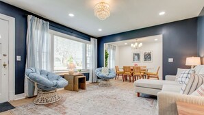 A modern living room with a blue accent wall, a chandelier, a dining area with a table and chairs, and a cozy seating area with a sofa and armchairs. - Modern 4BR Home Near MTSU and Restaurants (Murfreesboro)