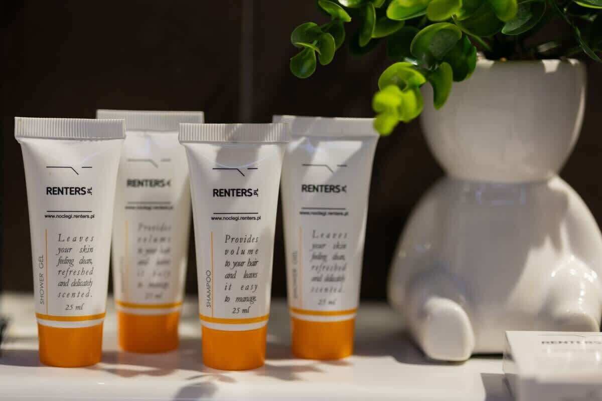 Quatre tubes de gel douche RENTERS® sont posés sur une étagère, avec un vase en céramique blanche et une plante verte en arrière-plan.