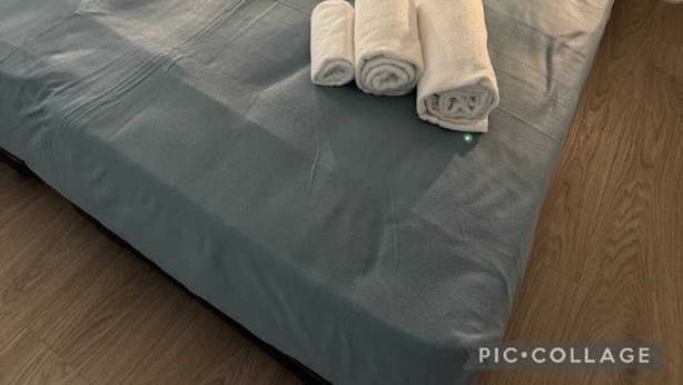 A neatly made bed with a grey bedspread, white pillows, and rolled white towels on the bed.