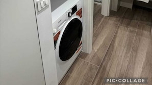 A laundry room with a front-loading washing machine, shelves, and a tiled floor.