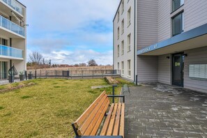 Moderni rakennus, jossa on tasainen julkisivu, nurmikkoalueella sijaitseva sisäpiha ja puinen penkki.