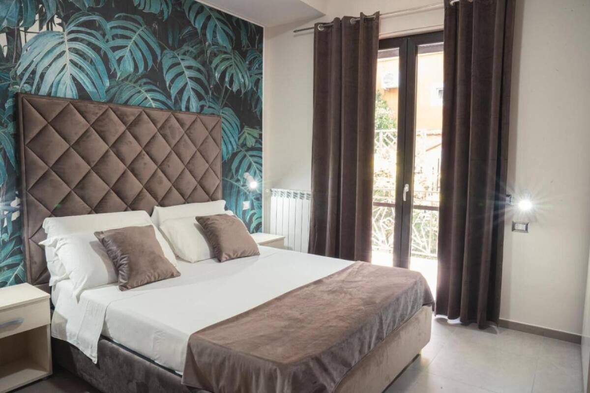 A bedroom with a large bed, a tufted headboard, and a view of the outdoors through a sliding door.
