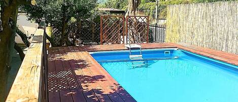 A wooden deck leading to a rectangular swimming pool with a metal ladder.
