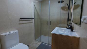 Un baño moderno con cabina de ducha de vidrio, inodoro blanco y tocador de madera con lavamanos.