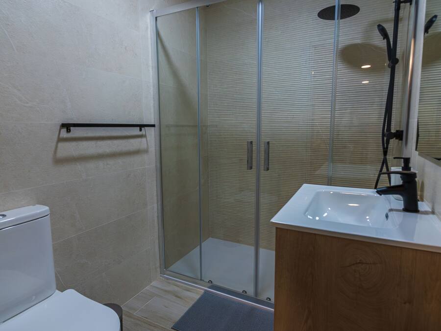 Un baño moderno con cabina de ducha de vidrio, inodoro blanco y tocador de madera con lavamanos.