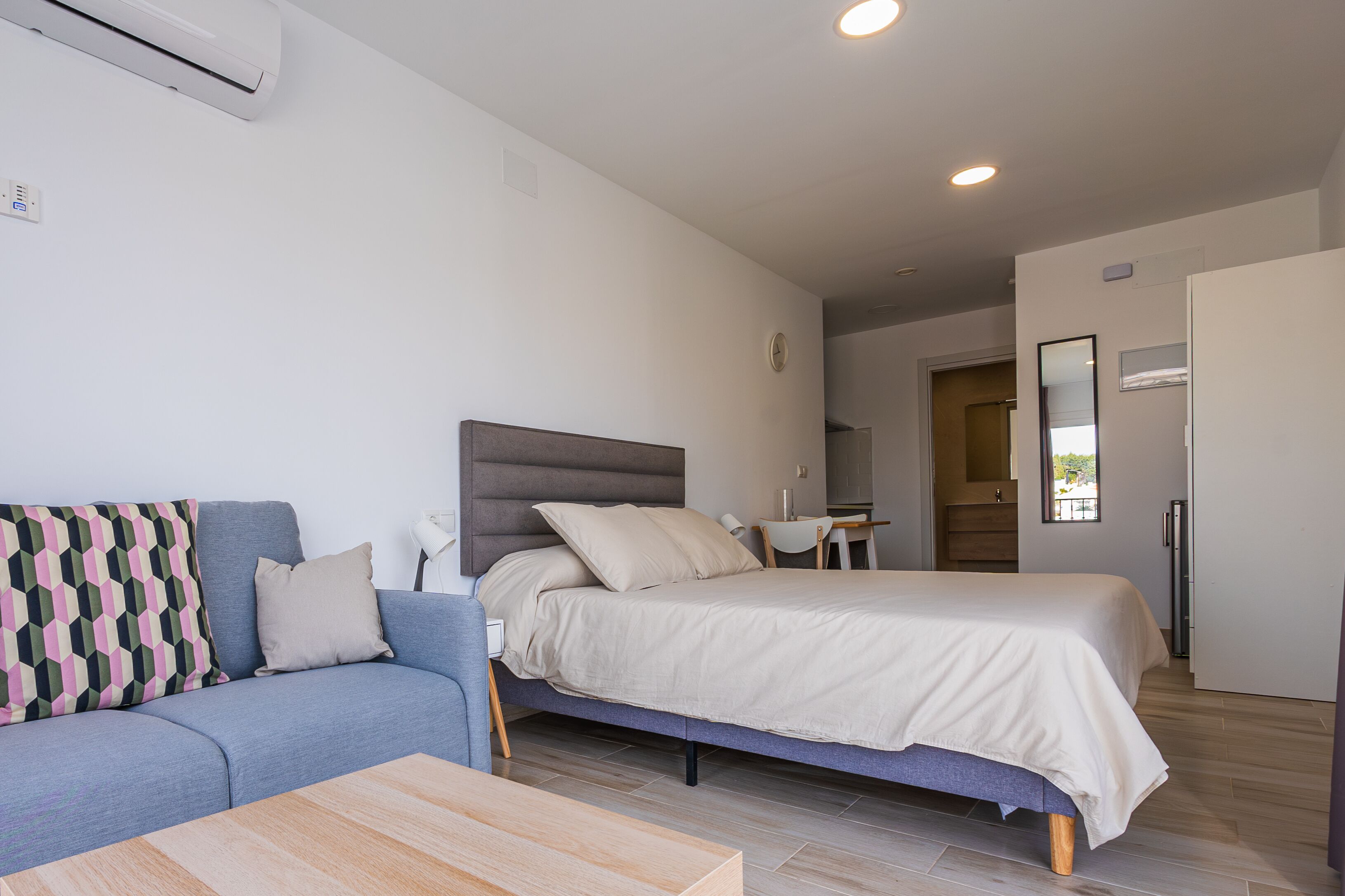 A modern bedroom with a bed, a sofa, a small table, and a mirror.