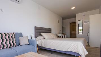 A modern bedroom with a bed, a sofa, a small table, and a mirror.