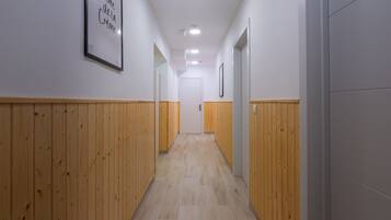 Un couloir aux murs recouverts de lambris en bois et au sol carrelé, qui mène à une porte blanche au fond.