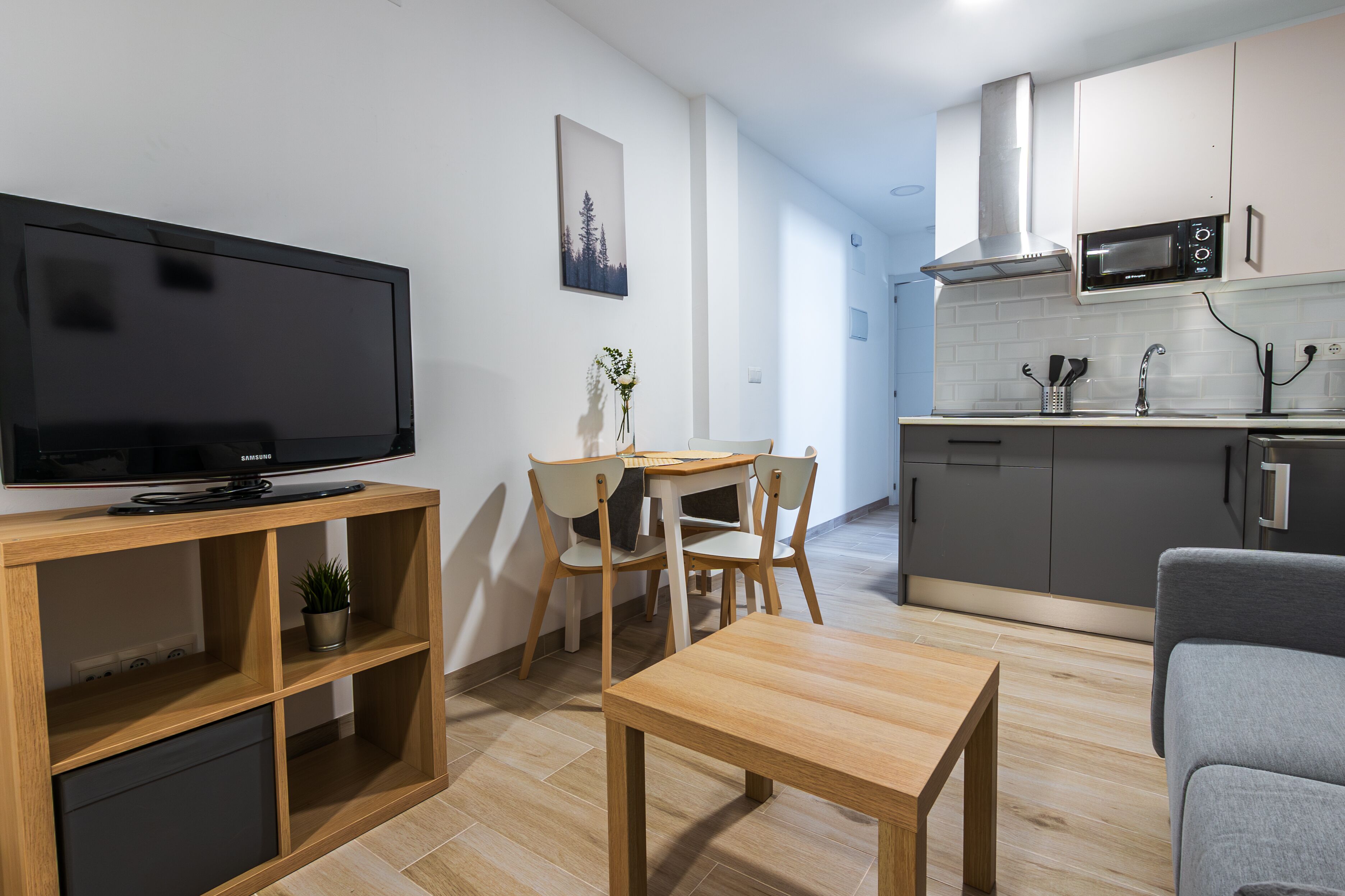 Una sala de estar moderna con un televisor de pantalla plana, muebles de madera, una mesa de comedor y un sofá gris.