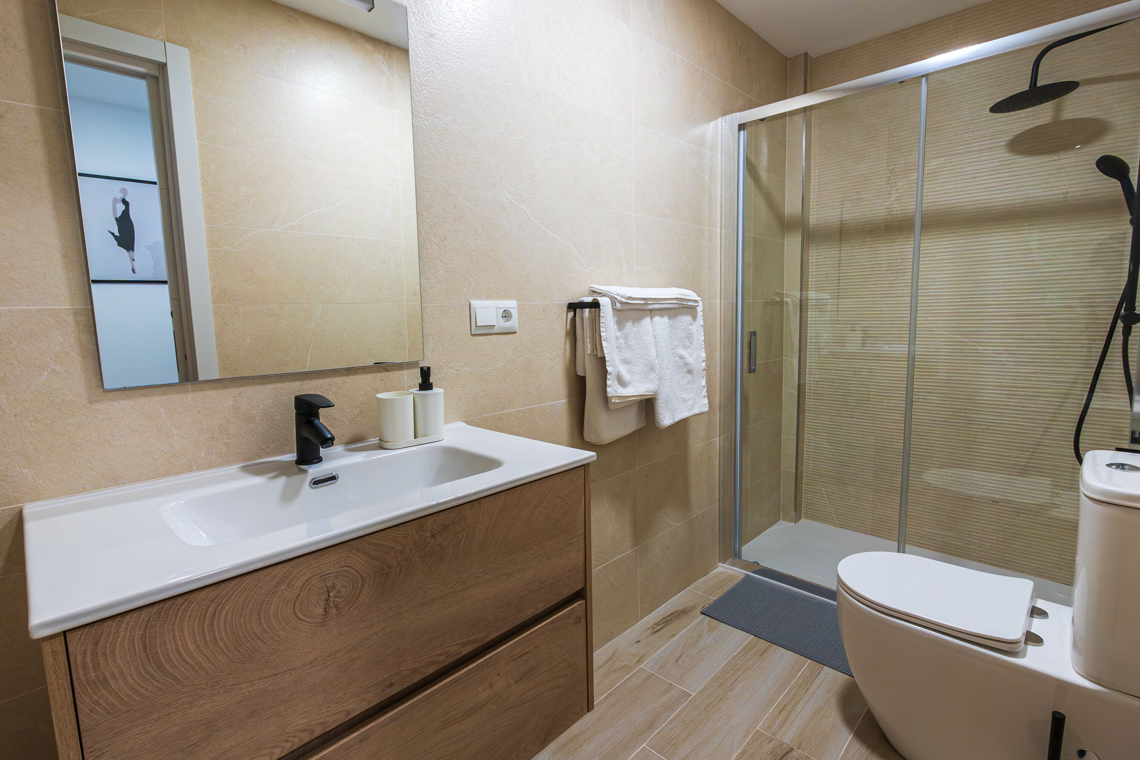 A modern bathroom with a wooden vanity, a glass shower enclosure, and a toilet.