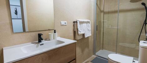 A modern bathroom with a wooden vanity, a glass shower enclosure, and a toilet.