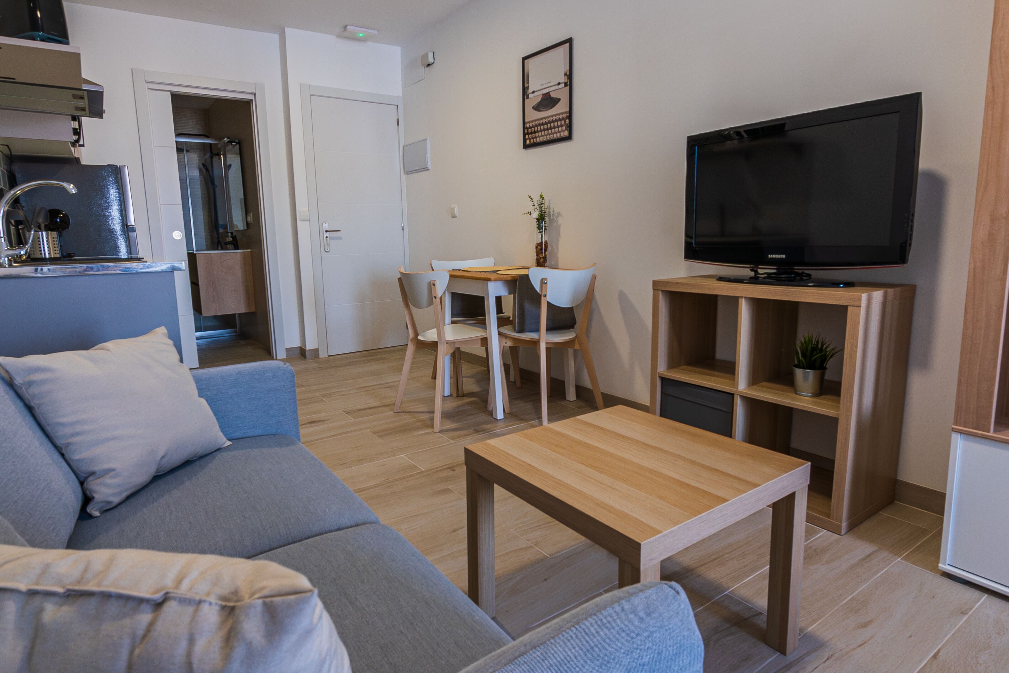 Een woonkamer met een bank, een salontafel, een televisie en een eethoek met stoelen en een tafel.