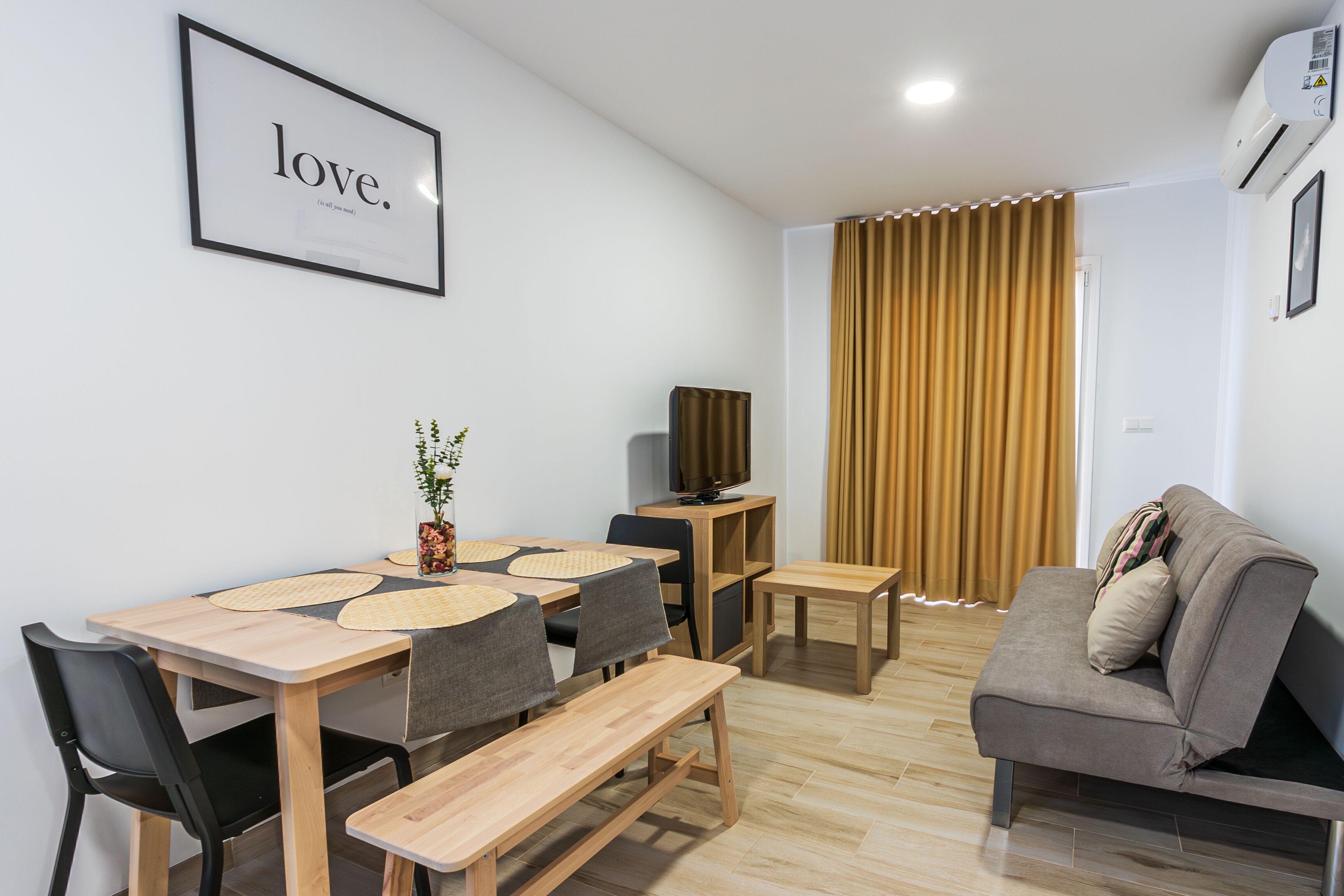 A modern living room with a dining area, a sofa, and a television.