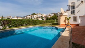 A swimming pool with a geometric tile pattern, surrounded by a patio area with a satellite dish and a white building with a window and a door. - Apartamentos turisticos Jose Cruz  (Nerja)