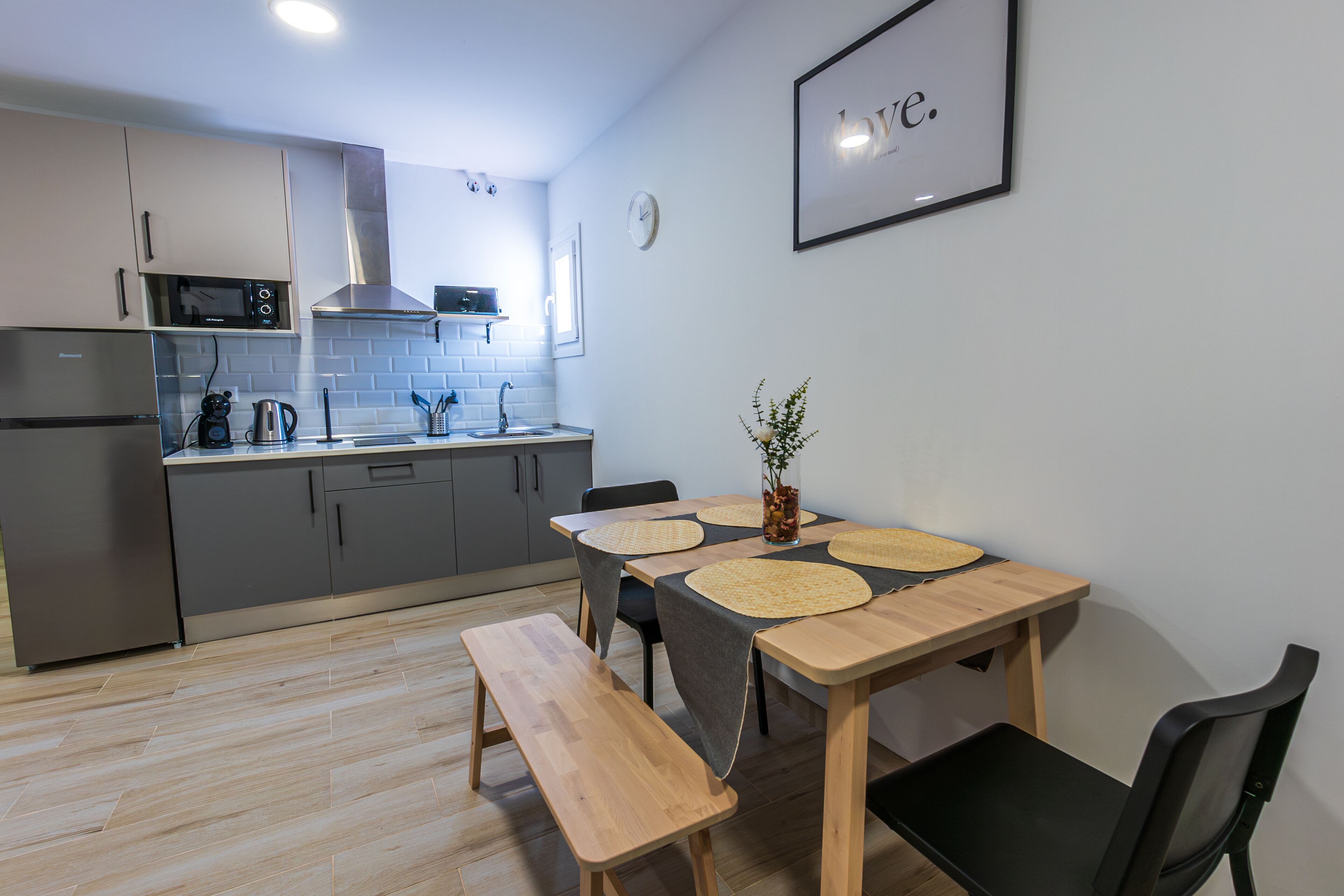 A modern kitchen with a wooden table, chairs, a bench, and a clock on the wall.