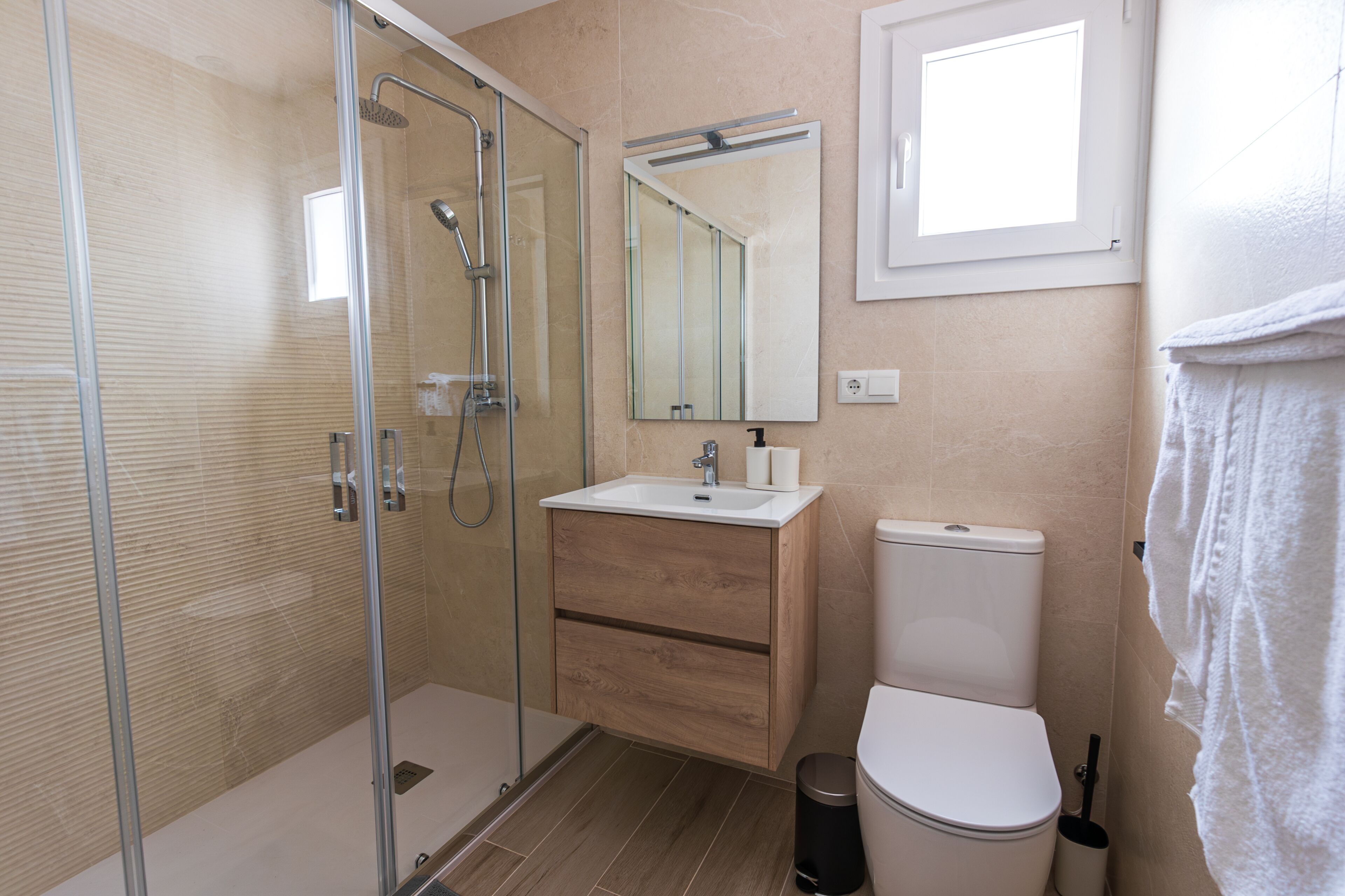 A modern bathroom with a glass-enclosed shower, a wooden vanity, a white toilet, and a large mirror.