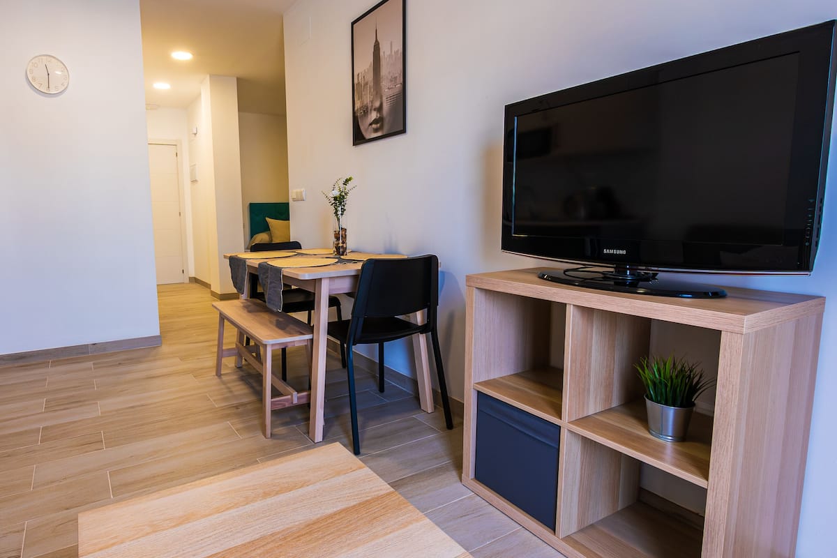 A modern living room with a flat-screen TV, wooden furniture, and a small plant on a shelf.