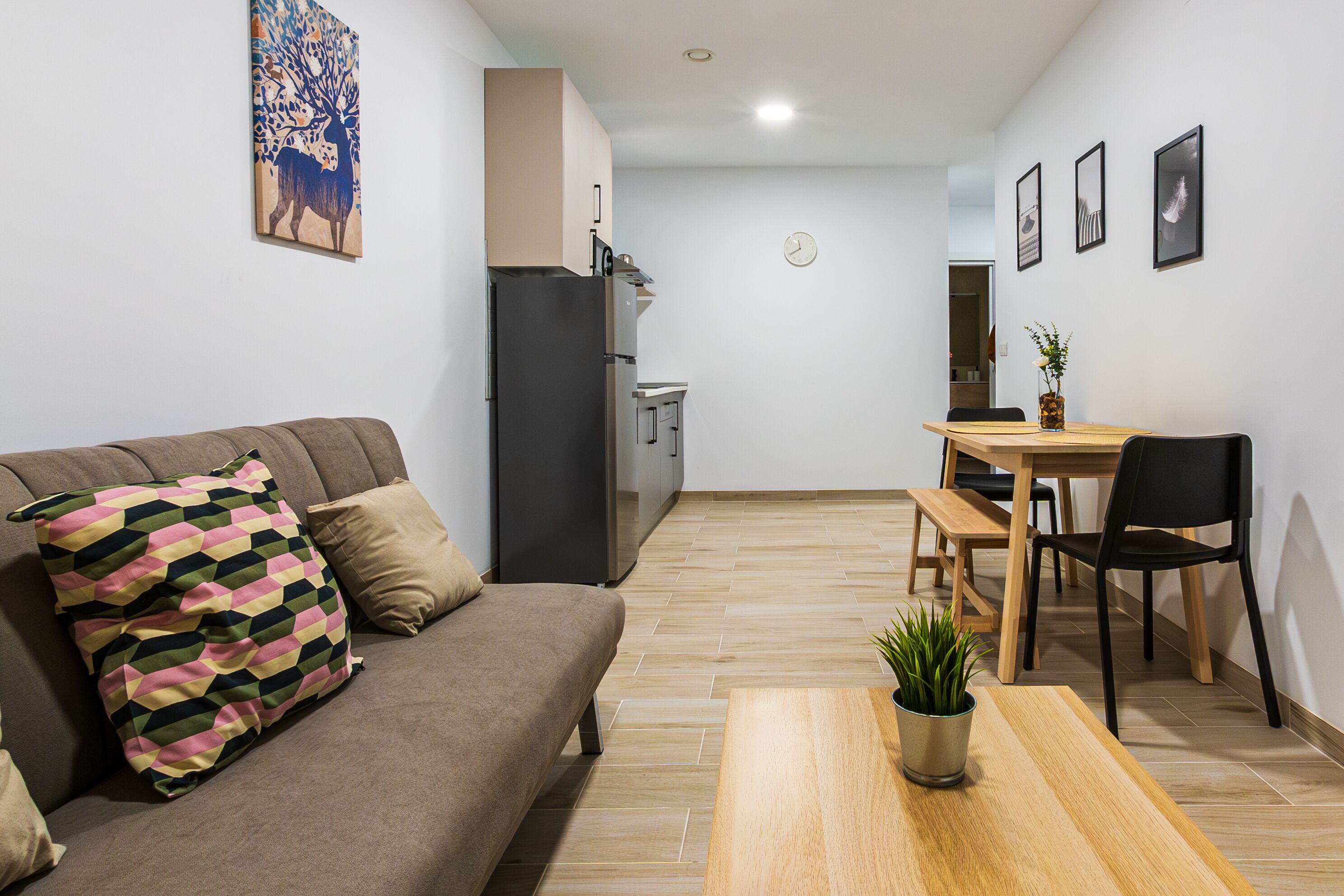 A modern living room with a sofa, a dining table, and a kitchen in the background.