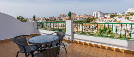 Une terrasse avec une table ronde et quatre chaises, un sol carrelé et une vue sur un quartier résidentiel avec des immeubles et de la verdure.