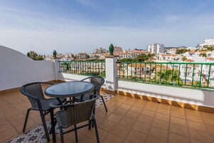 Eine Terrasse mit einem runden Tisch und vier Stühlen, einem Fliesenboden und Blick auf eine Wohngegend mit Gebäuden und Grünflächen.