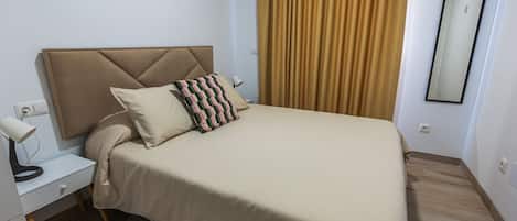 A neatly made bed with a headboard, a bedside table with a lamp, and a mirror on the wall.