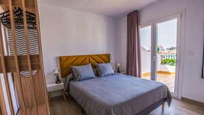 A modern bedroom with a wooden headboard, a grey bedspread, and a nightstand with a lamp. - Apartamentos turisticos Jose Cruz  (Nerja)