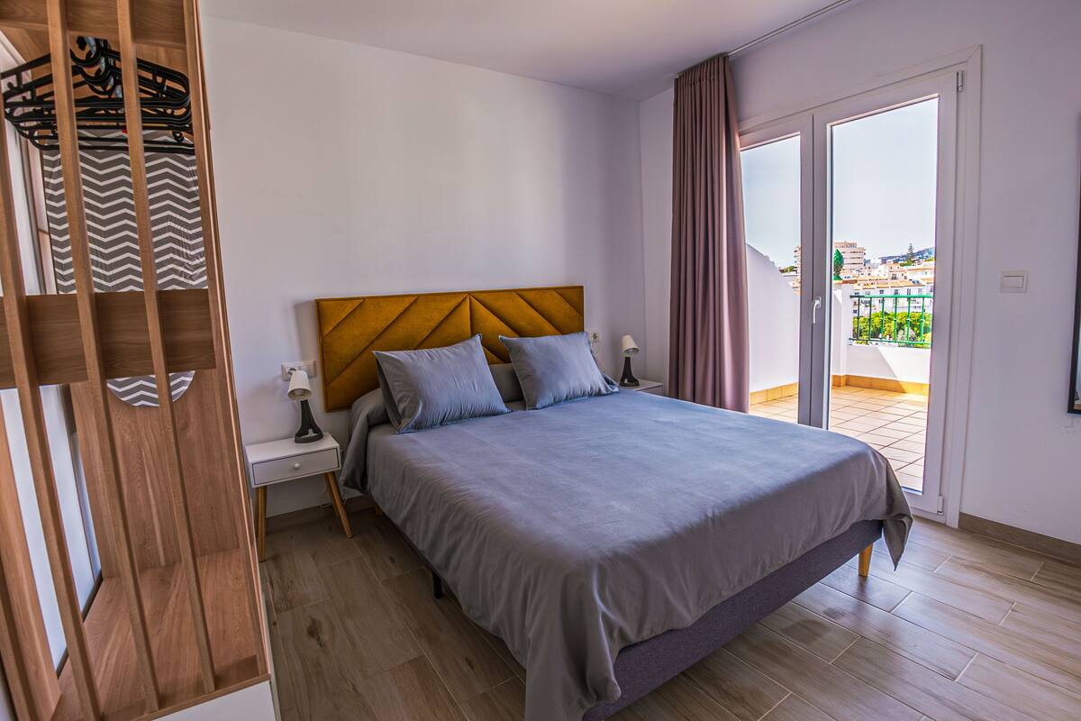 A modern bedroom with a wooden headboard, a grey bedspread, and a nightstand with a lamp.