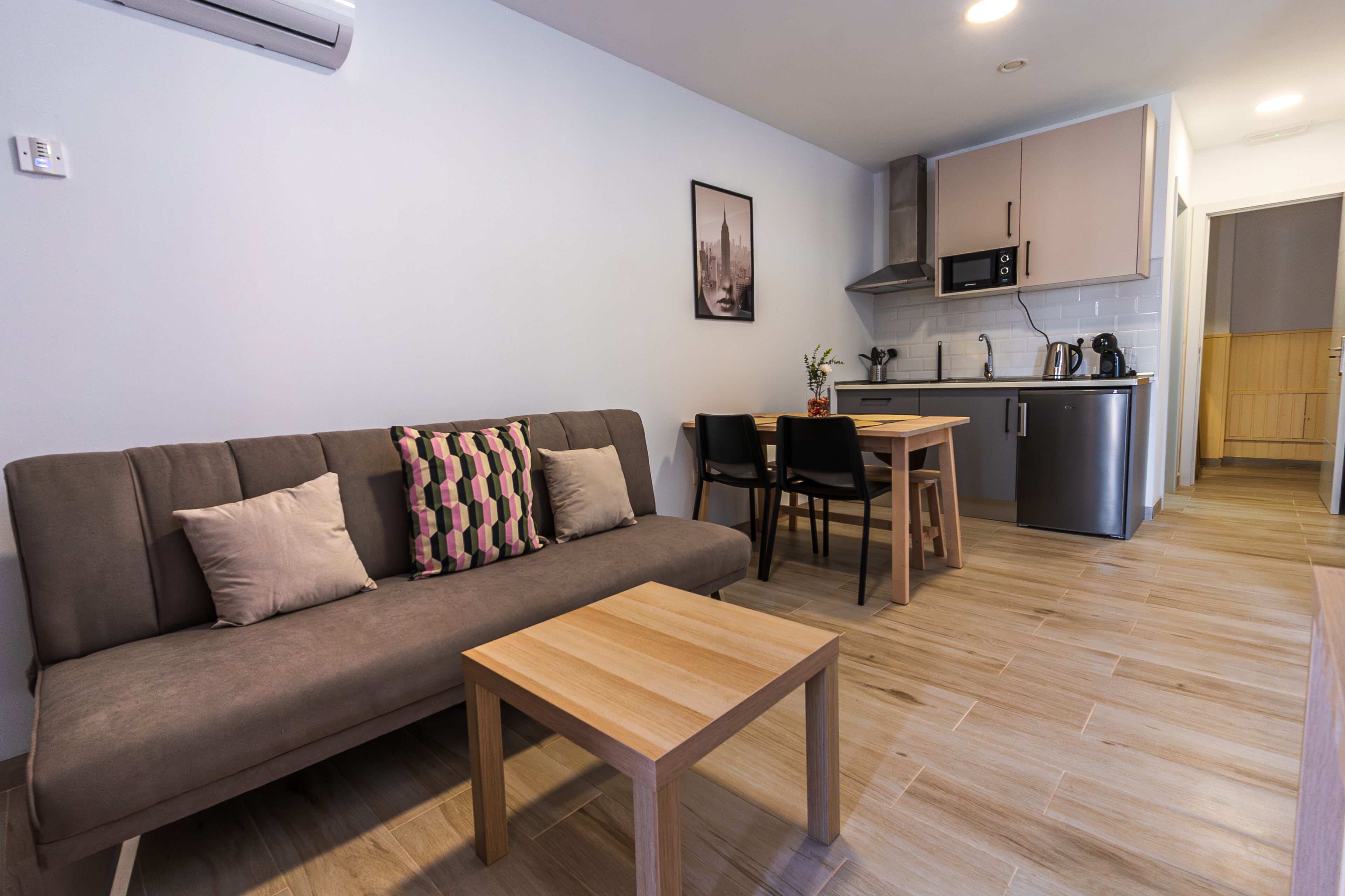 A modern living room with a sofa, a wooden coffee table, and a dining area with a small kitchen in the background.