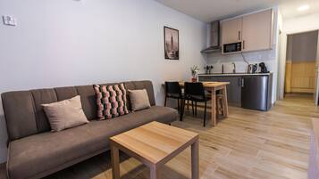 A modern living room with a sofa, a wooden coffee table, and a dining area with a small kitchen in the background.