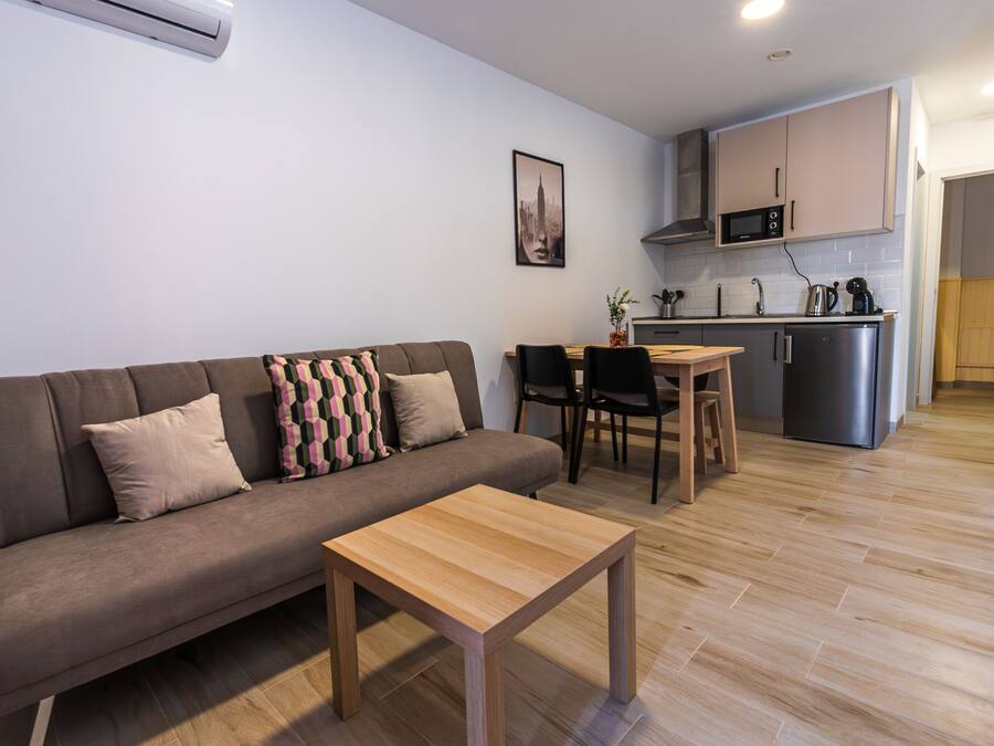 Una sala de estar moderna con un sofá, una mesa de centro de madera y una zona de comedor con una pequeña cocina al fondo.