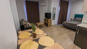 A modern hotel room with a wooden dining table, a sofa, a TV, and a small cabinet.