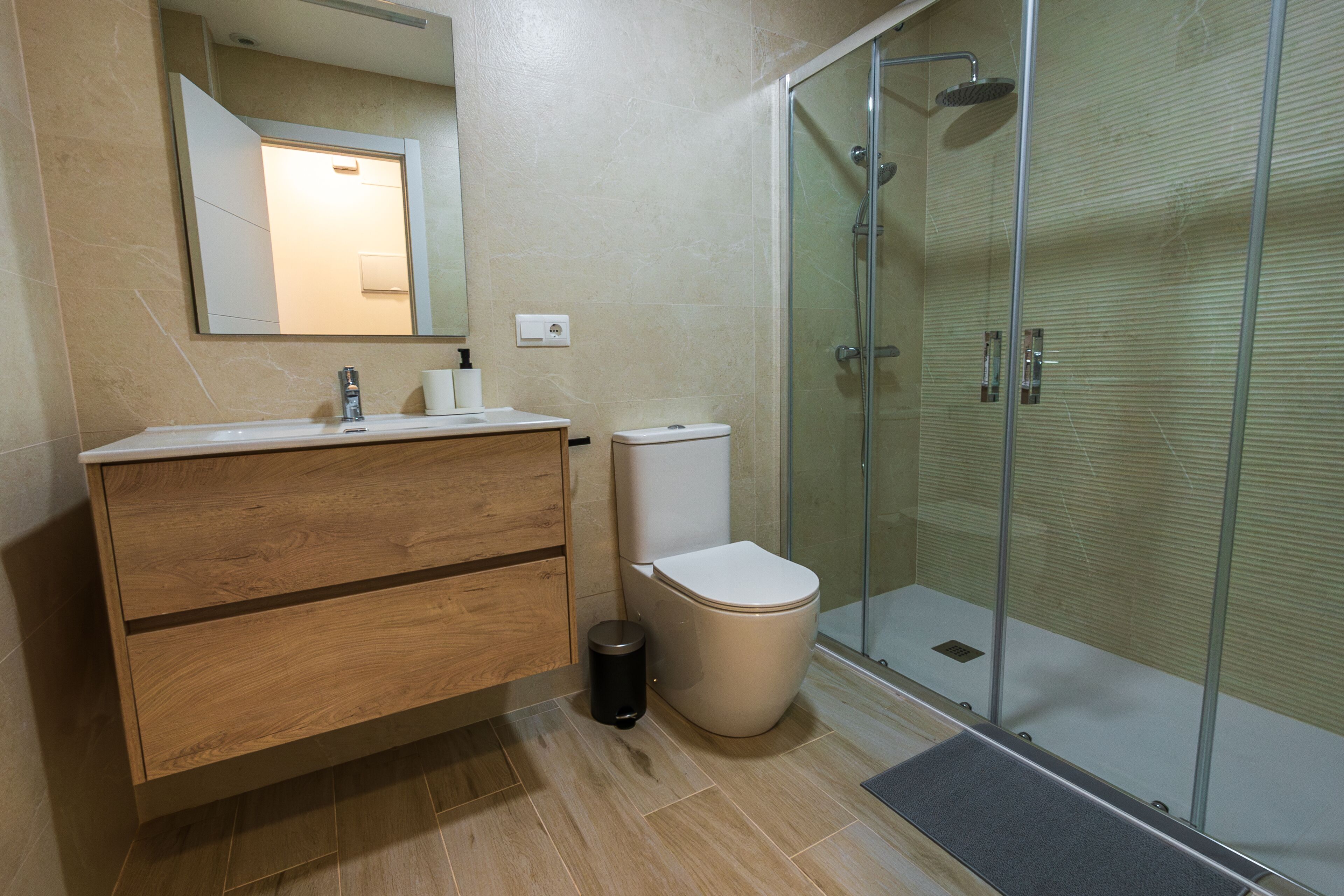 A modern bathroom with a wooden vanity, a toilet, and a glass-enclosed shower.