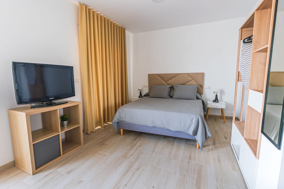 A modern bedroom with a bed, a TV on a wooden stand, a nightstand, and a wardrobe.