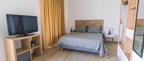Un dormitorio moderno con cama, televisor sobre un mueble de madera, mesita de noche y armario.