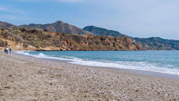 A pebbly beach with rocky cliffs and mountains in the background. - Apartamentos turisticos Jose Cruz  (Nerja)