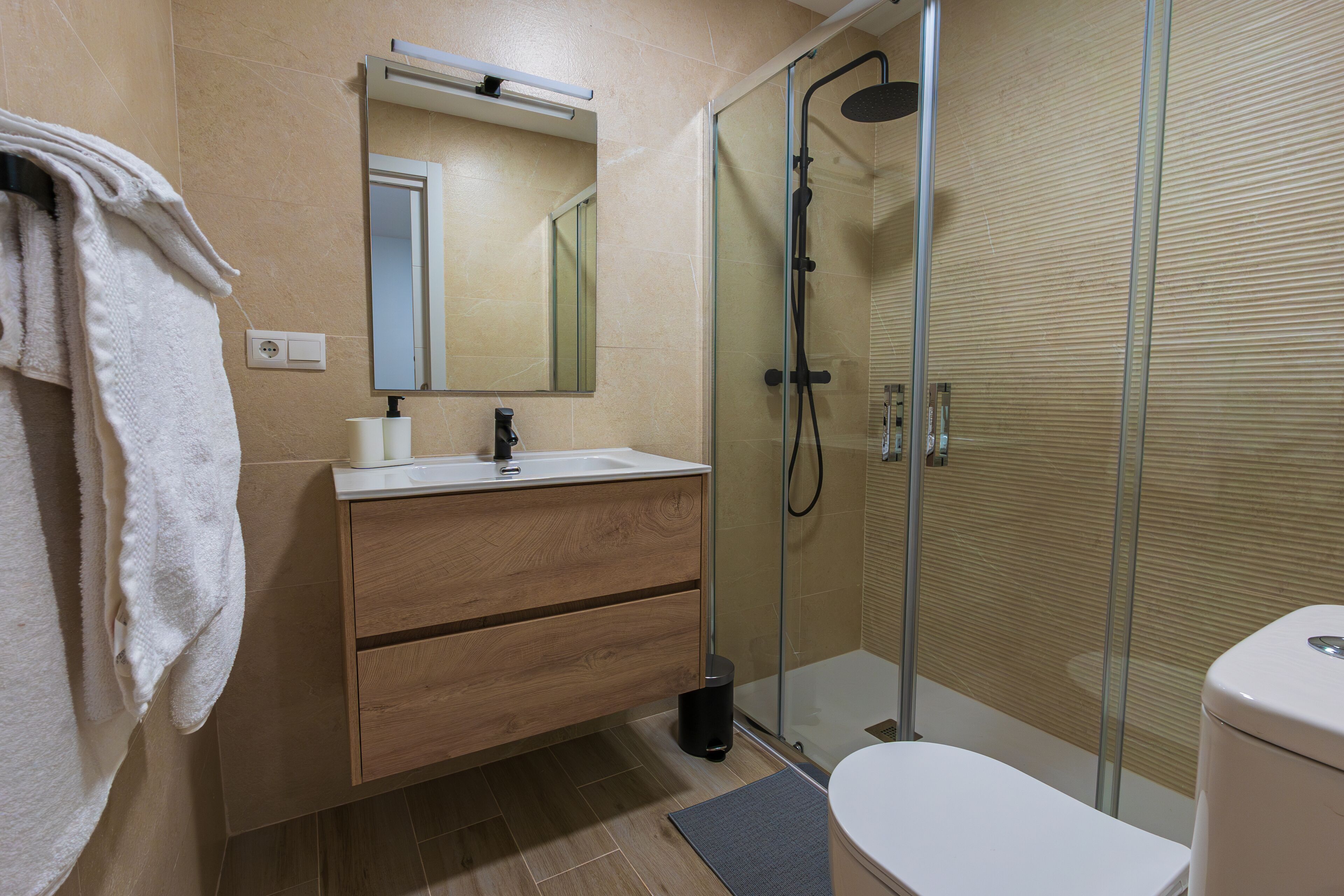 Un bany modern amb una cabina de dutxa de vidre, un moble de tocador de fusta i un vàter blanc.