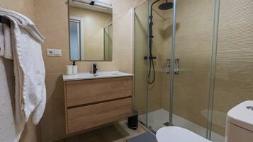 Un bany modern amb una cabina de dutxa de vidre, un moble de tocador de fusta i un vàter blanc.