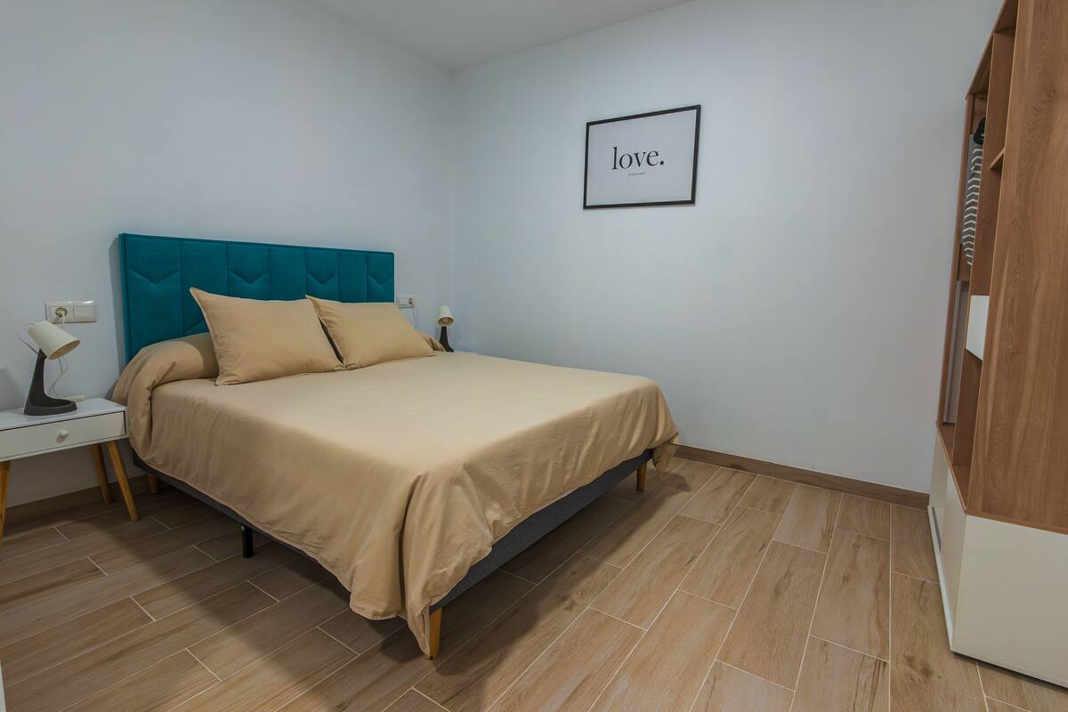 A bedroom with a bed, a nightstand, a lamp, and a framed picture on the wall.